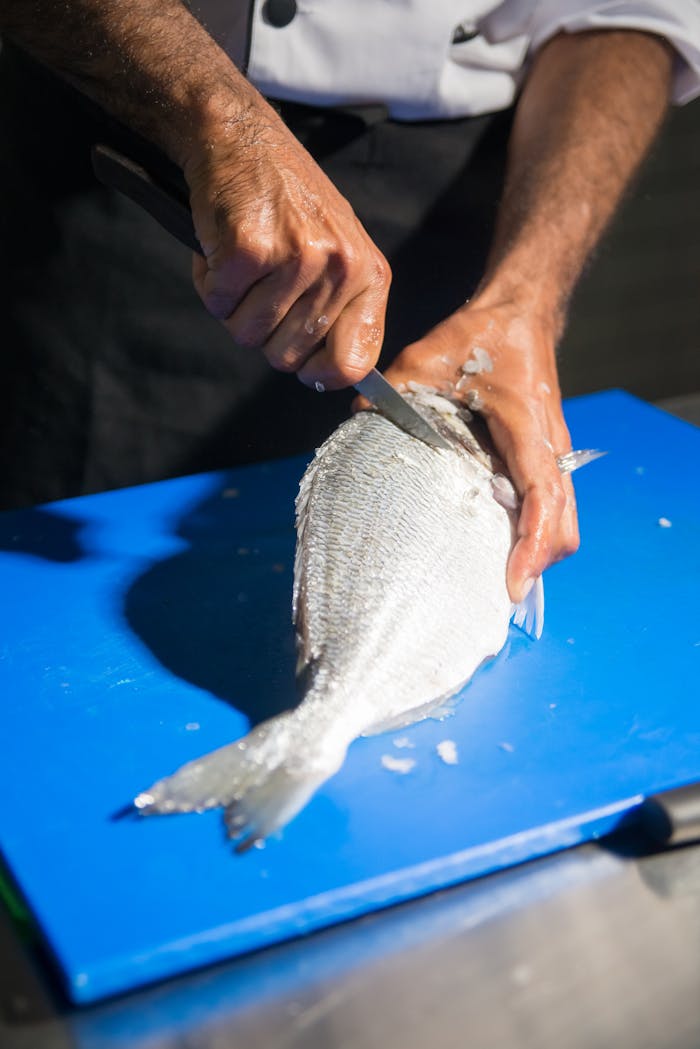 gallery-1 Chef skillfully filleting a fish on a blue cutting board, demonstrating culinary expertise.
