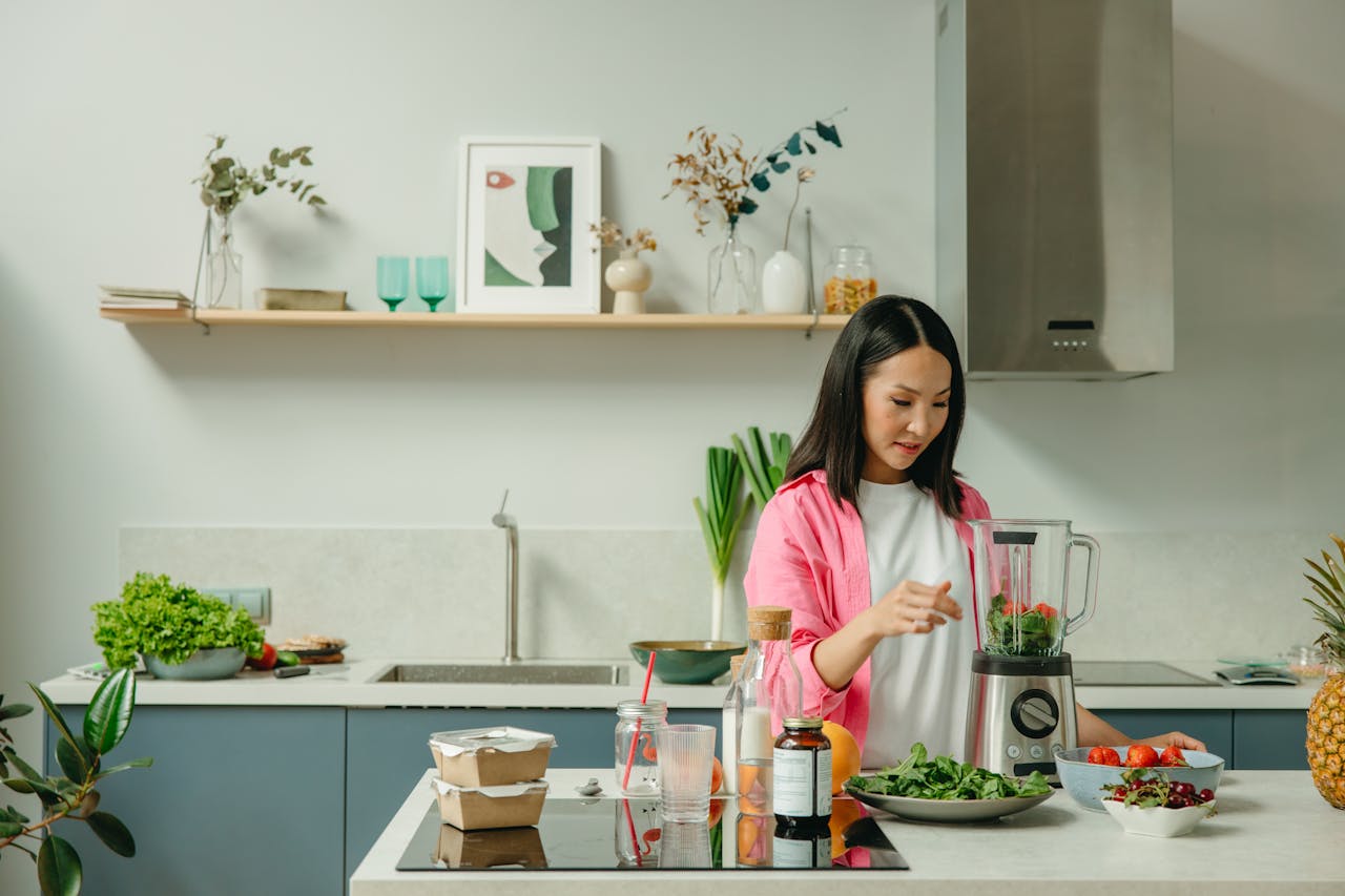 our-services-2 Asian woman blending fresh fruits and vegetables in a stylish kitchen setting.